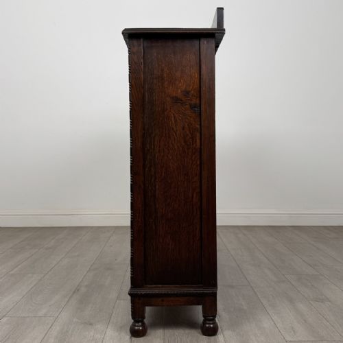 fig 2. A dark oak Jacobean style display cabinet featuring twin leaded glass doors, central carved bosses, internal shelving, and turned feet.
