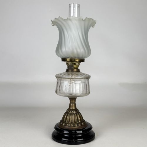 fig 1. A Victorian brass oil lamp with a black stepped base, a cut glass reservoir, an exposed glass chimney, and a swirled frosted glass shade with a ruffled rim.