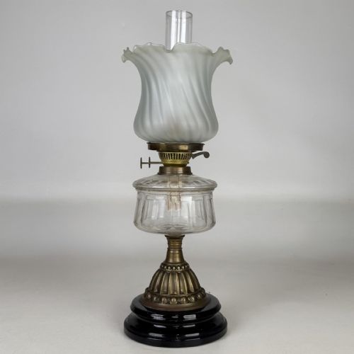 fig 2. A Victorian brass oil lamp with a black stepped base, a cut glass reservoir, an exposed glass chimney, and a swirled frosted glass shade with a ruffled rim.