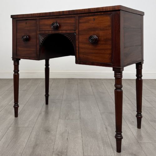 fig 1. A Regency mahogany kneehole sideboard featuring turned legs, flame mahogany drawer fronts, and fan-carved spandrel corner details.