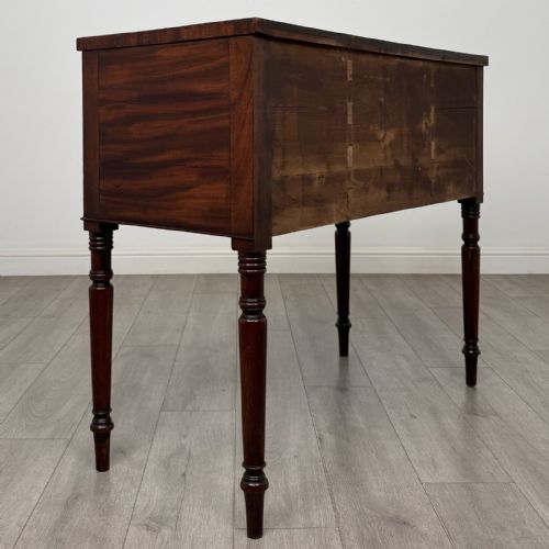 fig 3. A Regency mahogany kneehole sideboard featuring turned legs, flame mahogany drawer fronts, and fan-carved spandrel corner details.