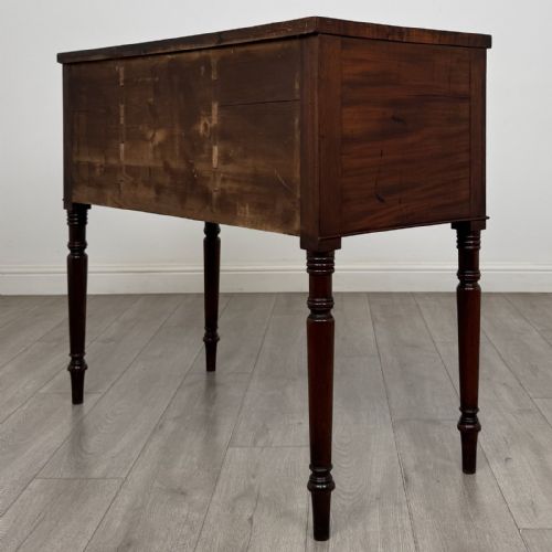 fig 5. A Regency mahogany kneehole sideboard featuring turned legs, flame mahogany drawer fronts, and fan-carved spandrel corner details.
