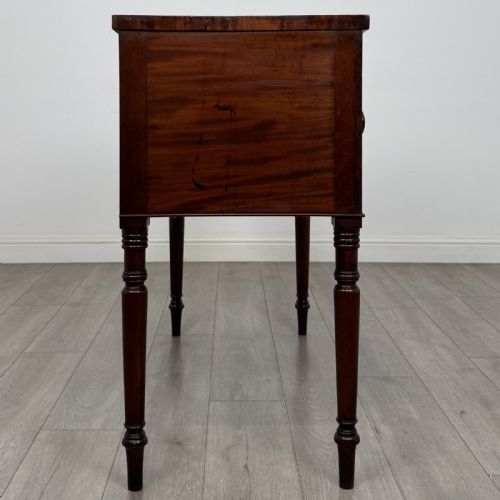 fig 6. A Regency mahogany kneehole sideboard featuring turned legs, flame mahogany drawer fronts, and fan-carved spandrel corner details.