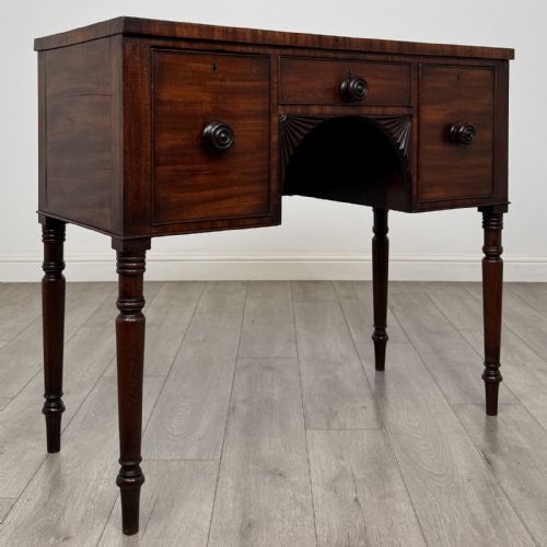 fig 7. A Regency mahogany kneehole sideboard featuring turned legs, flame mahogany drawer fronts, and fan-carved spandrel corner details.