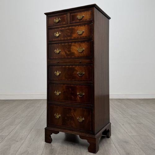 fig 1. A tall Georgian style mahogany chest of drawers featuring brass swan neck handles, a pull-out brushing slide, and bracket feet.