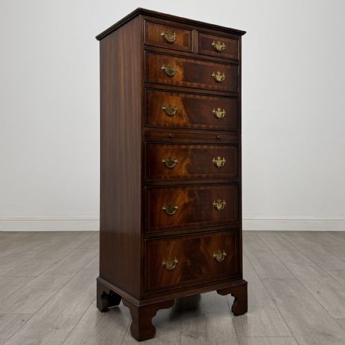 fig 7. A tall Georgian style mahogany chest of drawers featuring brass swan neck handles, a pull-out brushing slide, and bracket feet.