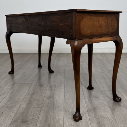 fig 5. A Queen Anne style walnut writing table featuring three drawers, decorative brass handles, carved cabriole legs, and a central shell motif on the lower apron.