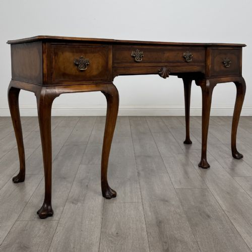 fig 7. A Queen Anne style walnut writing table featuring three drawers, decorative brass handles, carved cabriole legs, and a central shell motif on the lower apron.