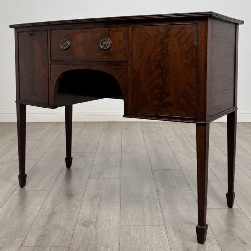 fig 1. A mahogany bowfront sideboard featuring two oval-inlaid cupboard doors flanking a central drawer, set upon four square tapered legs with spade feet.