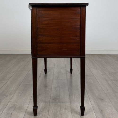 fig 2. A mahogany bowfront sideboard featuring two oval-inlaid cupboard doors flanking a central drawer, set upon four square tapered legs with spade feet.