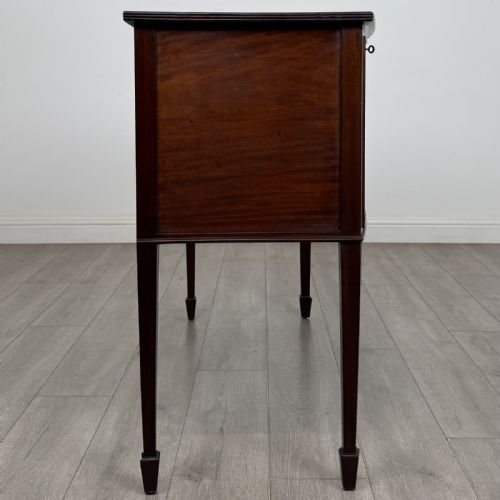 fig 6. A mahogany bowfront sideboard featuring two oval-inlaid cupboard doors flanking a central drawer, set upon four square tapered legs with spade feet.
