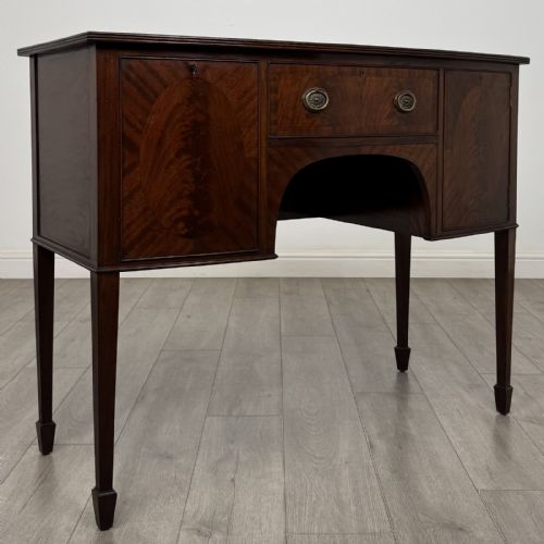 fig 7. A mahogany bowfront sideboard featuring two oval-inlaid cupboard doors flanking a central drawer, set upon four square tapered legs with spade feet.