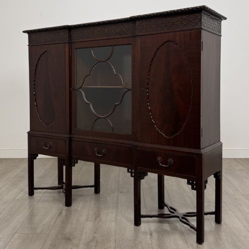 fig 1. An Edwardian dark mahogany breakfront cabinet featuring a central glazed door with geometric glazing bars flanked by two solid oval panel doors over three drawers and cross-stretched legs.