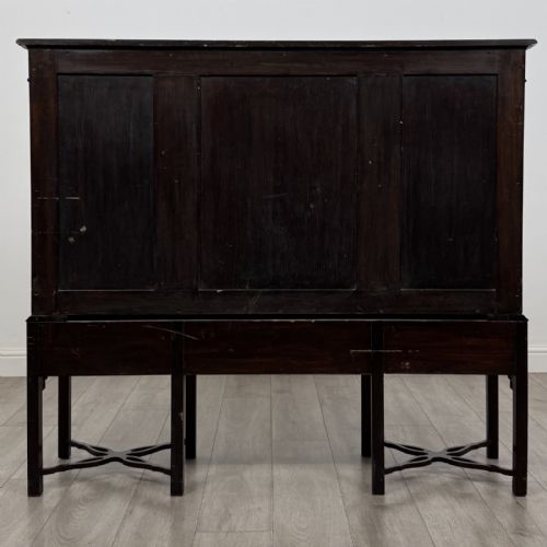 fig 4. An Edwardian dark mahogany breakfront cabinet featuring a central glazed door with geometric glazing bars flanked by two solid oval panel doors over three drawers and cross-stretched legs.