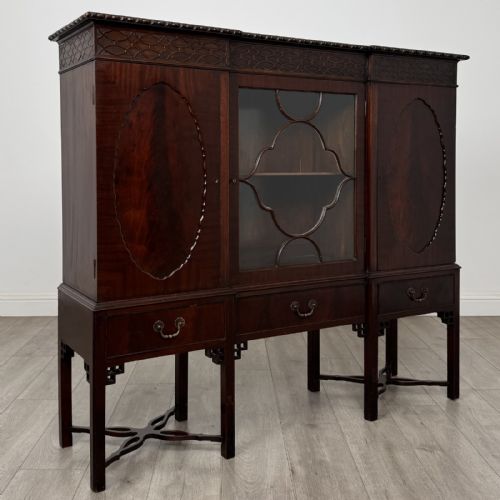 fig 7. An Edwardian dark mahogany breakfront cabinet featuring a central glazed door with geometric glazing bars flanked by two solid oval panel doors over three drawers and cross-stretched legs.