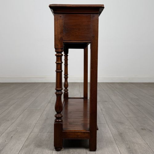fig 2. A narrow dark wood console table featuring two drawers with brass handles, turned front legs, and a lower potboard shelf.