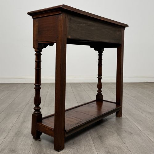 fig 3. A narrow dark wood console table featuring two drawers with brass handles, turned front legs, and a lower potboard shelf.