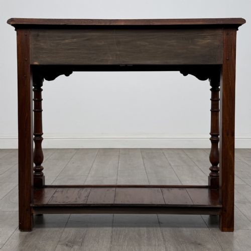 fig 4. A narrow dark wood console table featuring two drawers with brass handles, turned front legs, and a lower potboard shelf.