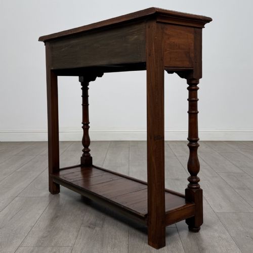 fig 5. A narrow dark wood console table featuring two drawers with brass handles, turned front legs, and a lower potboard shelf.