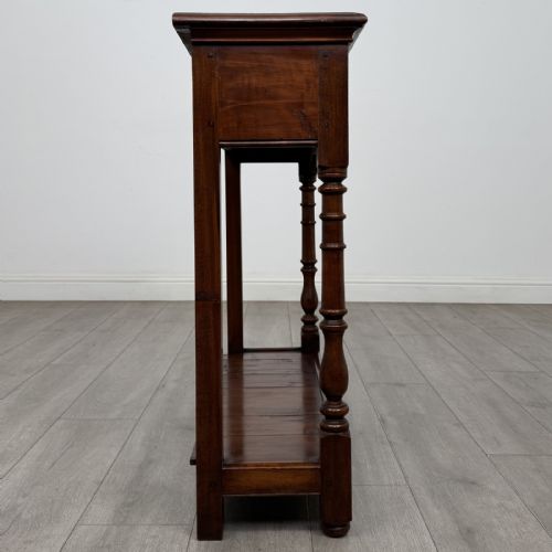 fig 6. A narrow dark wood console table featuring two drawers with brass handles, turned front legs, and a lower potboard shelf.