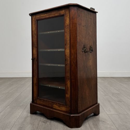 fig 1. A Victorian burr walnut music cabinet featuring a single glazed door revealing internal shelves with gilt-embossed text labels.