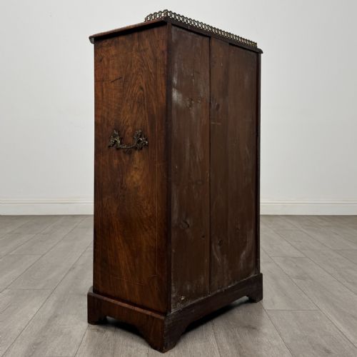 fig 3. A Victorian burr walnut music cabinet featuring a single glazed door revealing internal shelves with gilt-embossed text labels.