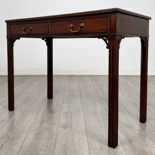 fig 1. A dark mahogany Chippendale style writing desk featuring two drawers with brass handles, straight fluted legs, and corner fretwork brackets.