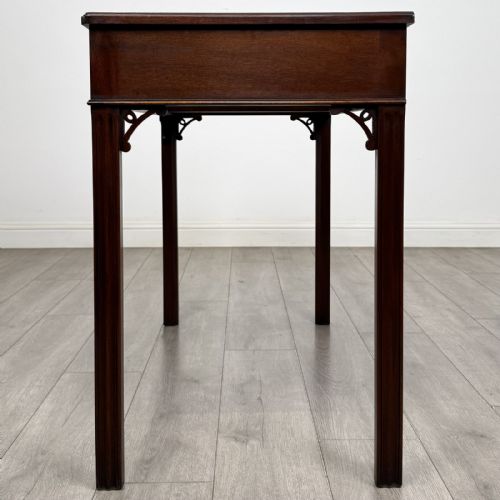 fig 2. A dark mahogany Chippendale style writing desk featuring two drawers with brass handles, straight fluted legs, and corner fretwork brackets.