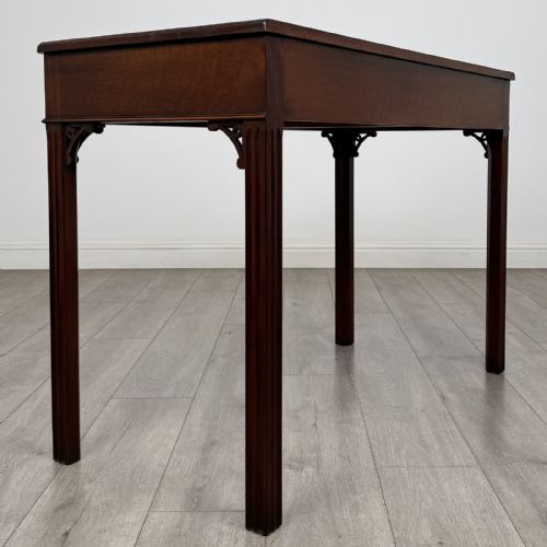 fig 3. A dark mahogany Chippendale style writing desk featuring two drawers with brass handles, straight fluted legs, and corner fretwork brackets.