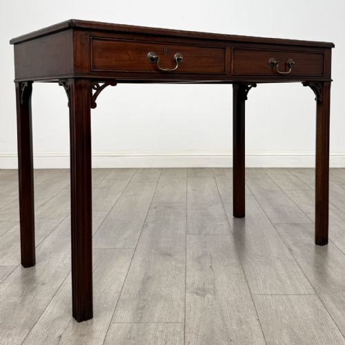 fig 7. A dark mahogany Chippendale style writing desk featuring two drawers with brass handles, straight fluted legs, and corner fretwork brackets.