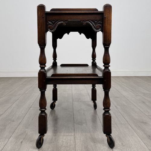 fig 2. A dark brown oak two-tier tea trolley featuring turned supports, carved corner spandrels, and metal castors on the feet.
