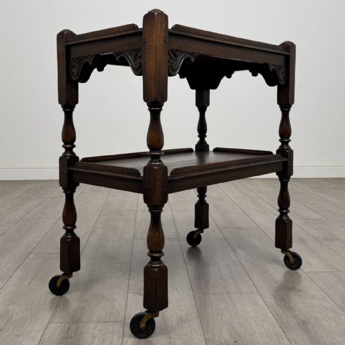 fig 3. A dark brown oak two-tier tea trolley featuring turned supports, carved corner spandrels, and metal castors on the feet.