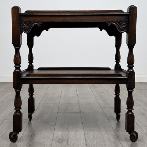 fig 4. A dark brown oak two-tier tea trolley featuring turned supports, carved corner spandrels, and metal castors on the feet.