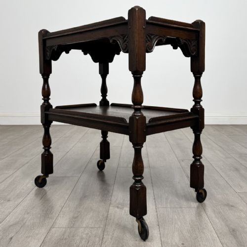 fig 5. A dark brown oak two-tier tea trolley featuring turned supports, carved corner spandrels, and metal castors on the feet.