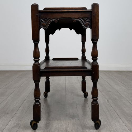 fig 6. A dark brown oak two-tier tea trolley featuring turned supports, carved corner spandrels, and metal castors on the feet.
