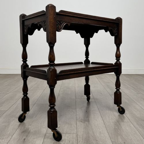fig 7. A dark brown oak two-tier tea trolley featuring turned supports, carved corner spandrels, and metal castors on the feet.