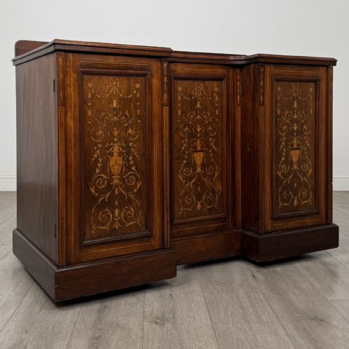 fig 7. A dark rosewood Victorian breakfront sideboard with three cupboard doors featuring intricate satinwood urn and scroll marquetry inlays.
