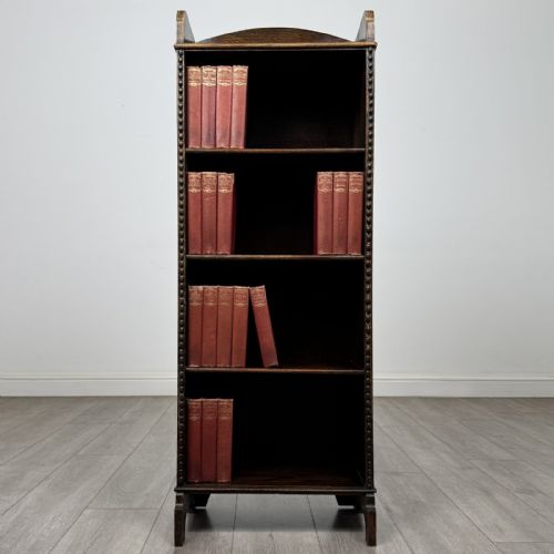 fig 1. A tall, narrow dark oak open bookcase featuring four fixed shelves, beaded front stiles, and a low arched top gallery rail.