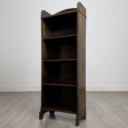 fig 2. A tall, narrow dark oak open bookcase featuring four fixed shelves, beaded front stiles, and a low arched top gallery rail.