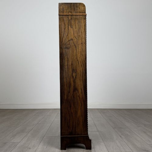fig 7. A tall, narrow dark oak open bookcase featuring four fixed shelves, beaded front stiles, and a low arched top gallery rail.