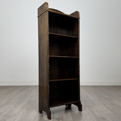 fig 8. A tall, narrow dark oak open bookcase featuring four fixed shelves, beaded front stiles, and a low arched top gallery rail.