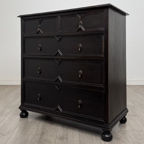 fig 1. An ebonised oak chest of drawers featuring geometric moulded panel fronts, brass drop handles, and turned bun feet.