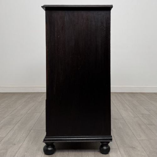 fig 2. An ebonised oak chest of drawers featuring geometric moulded panel fronts, brass drop handles, and turned bun feet.