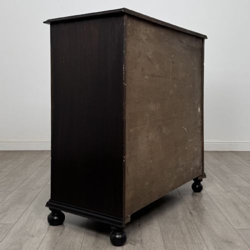 fig 3. An ebonised oak chest of drawers featuring geometric moulded panel fronts, brass drop handles, and turned bun feet.