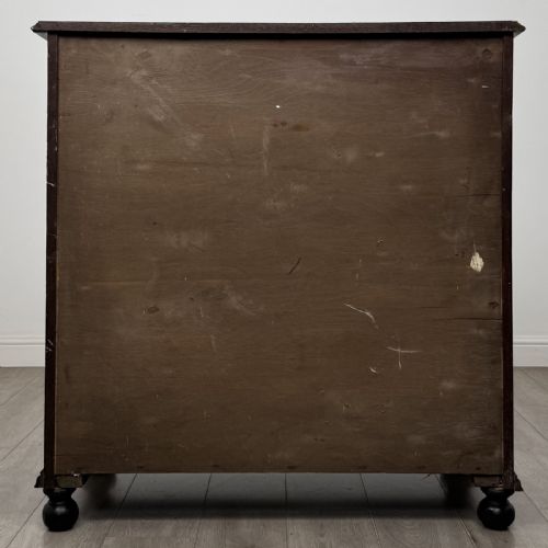 fig 4. An ebonised oak chest of drawers featuring geometric moulded panel fronts, brass drop handles, and turned bun feet.