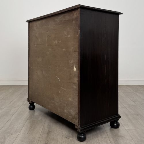 fig 5. An ebonised oak chest of drawers featuring geometric moulded panel fronts, brass drop handles, and turned bun feet.