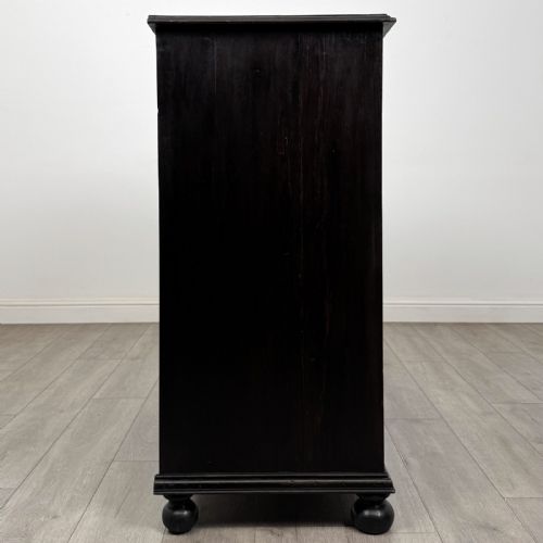 fig 6. An ebonised oak chest of drawers featuring geometric moulded panel fronts, brass drop handles, and turned bun feet.