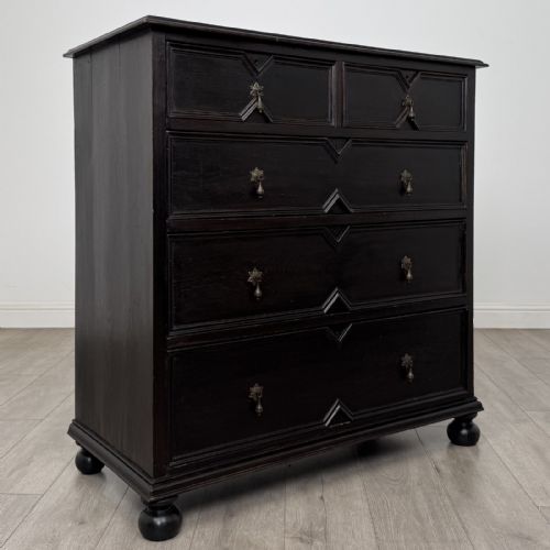 fig 7. An ebonised oak chest of drawers featuring geometric moulded panel fronts, brass drop handles, and turned bun feet.
