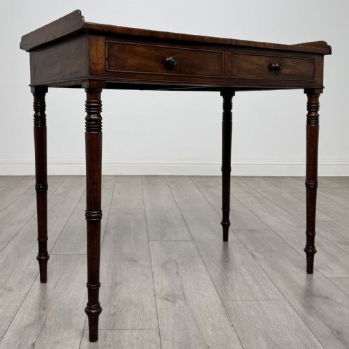 fig 7. An antique dark mahogany Regency writing table featuring two front drawers with turned wooden knobs and four tapered ring-turned legs.