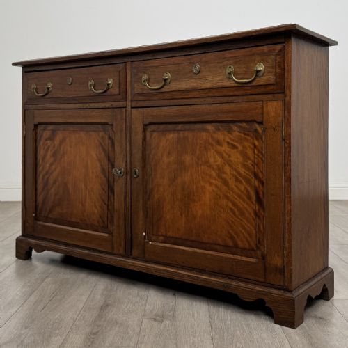 fig 1. A Georgian style warm brown oak dresser base featuring two drawers with brass drop handles above two panelled cupboard doors, raised on bracket feet.